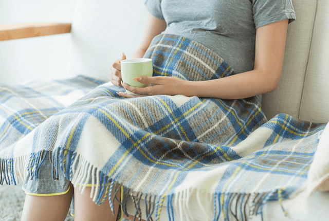 ブランケットをかけて飲み物をのむ妊婦さん